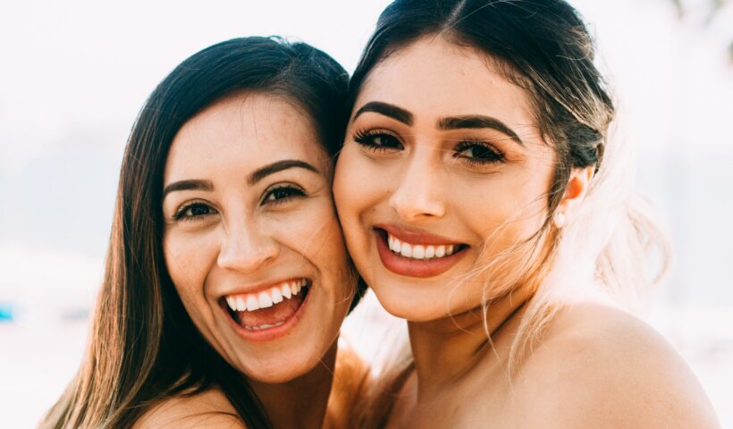 2 smiling women smiling in front of white background